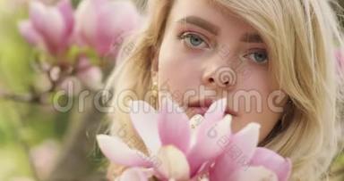 一位年轻迷人的女人的肖像，她有一头华丽的<strong>金色头发</strong>，在粉红色花瓣的花树之间。 可爱的金发美女